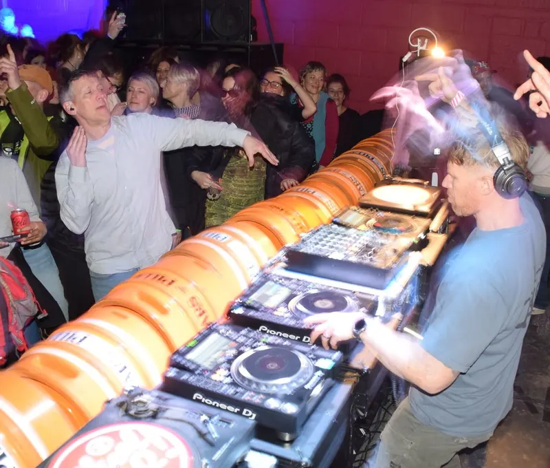 Bring The Beat Mack DJing behind a booth of orange kegs while the crowd dances