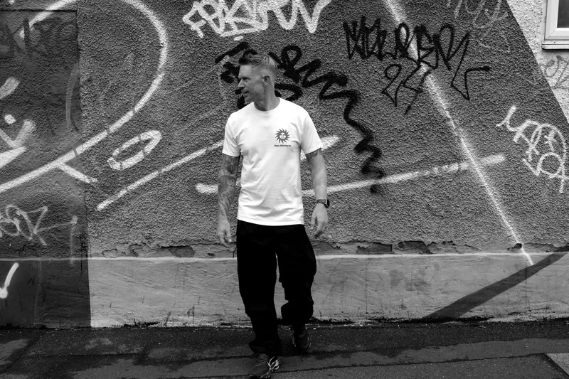 Black and white shot of Bring The Beat Mack walking past a graffiti wall